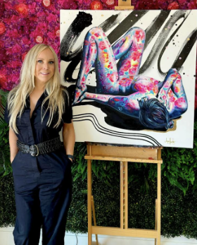 Blond woman standing in front of painting of woman with color pink blue on her body