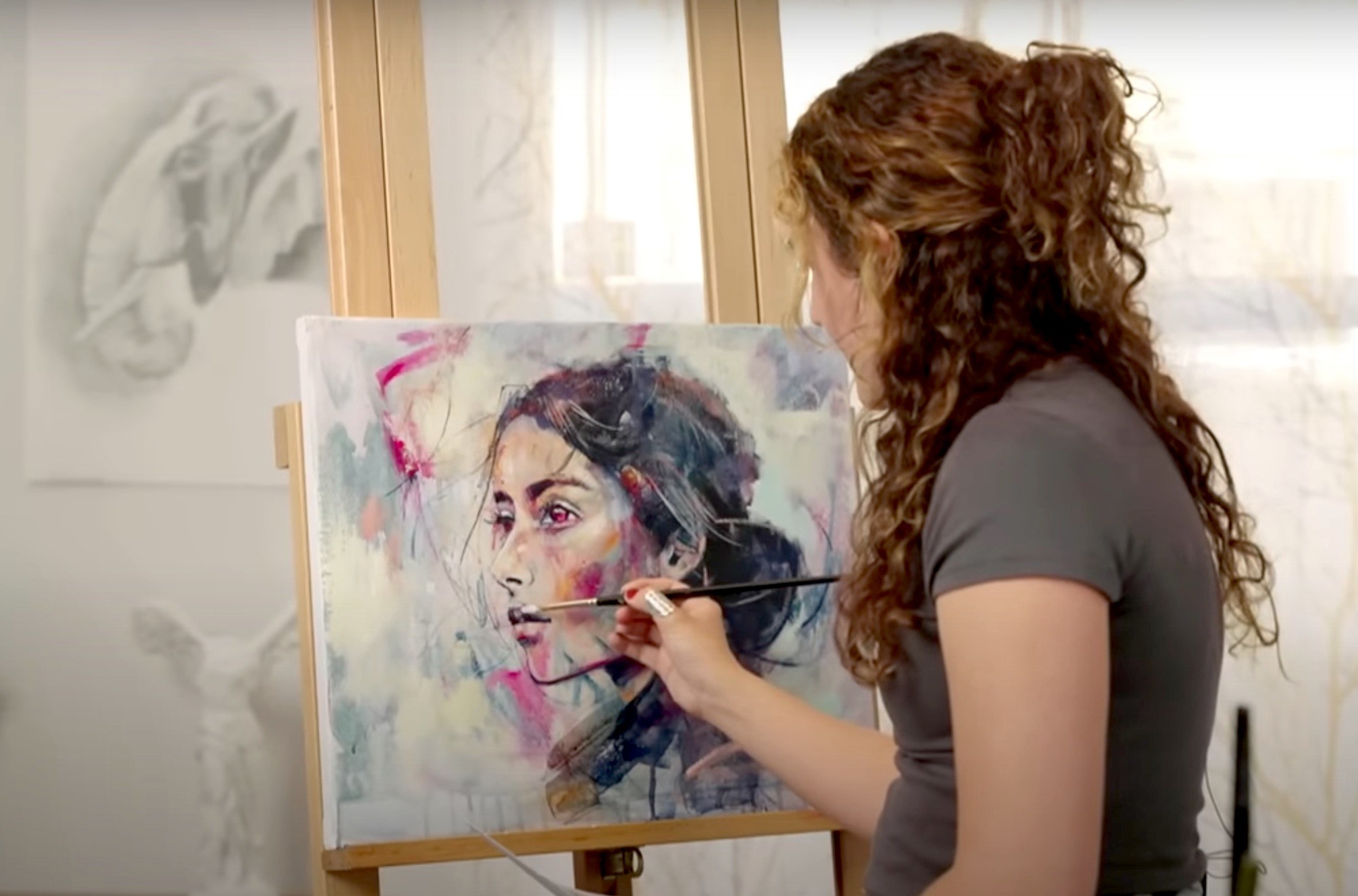 girl in brown hair painting a portrait on a cream and grey canvas