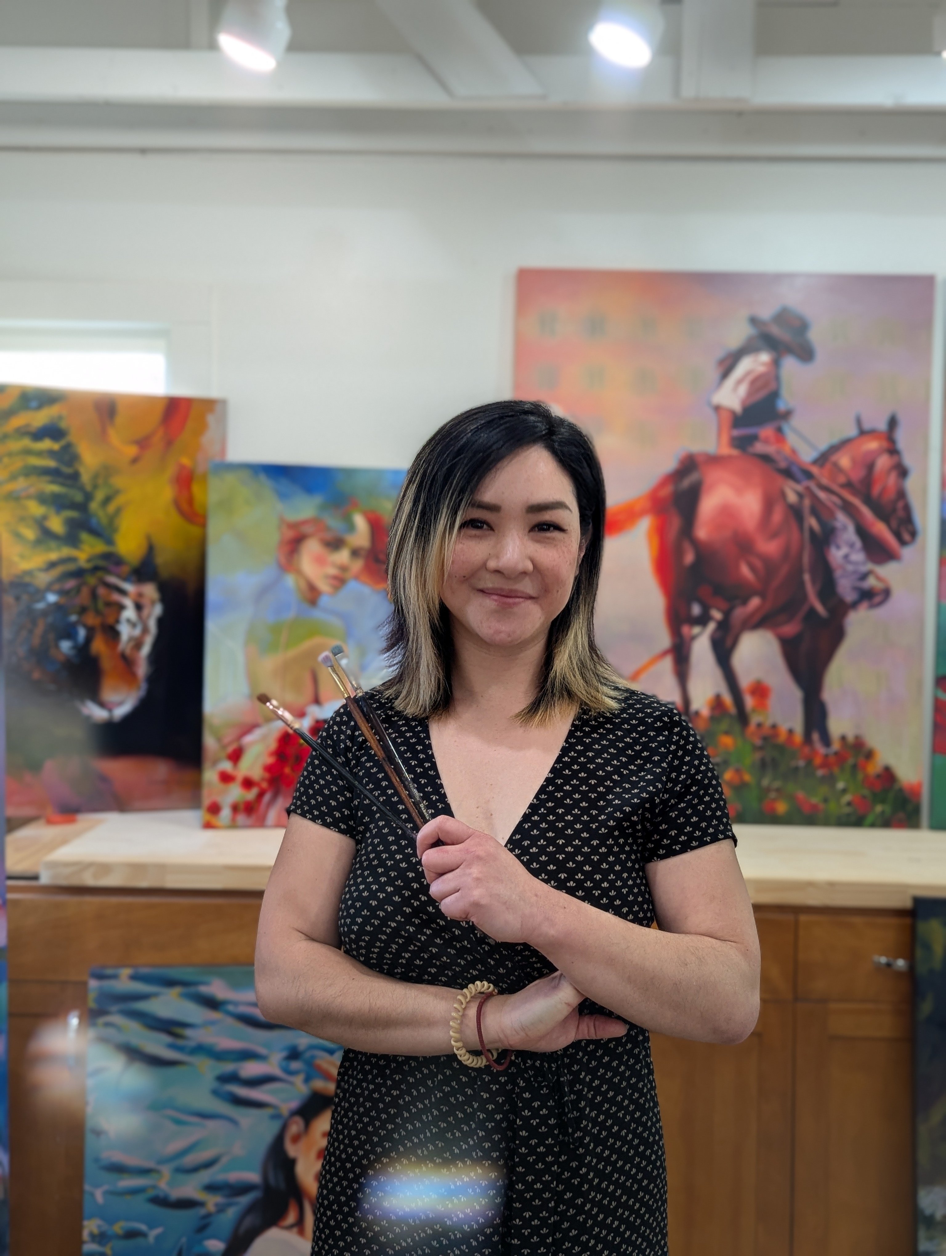 Female artist holding paintbrush in front of art 