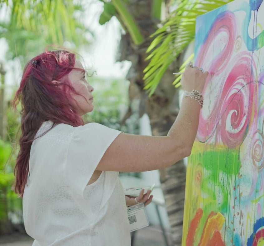 Woman painting outside on canvas pink swirl green orange paint