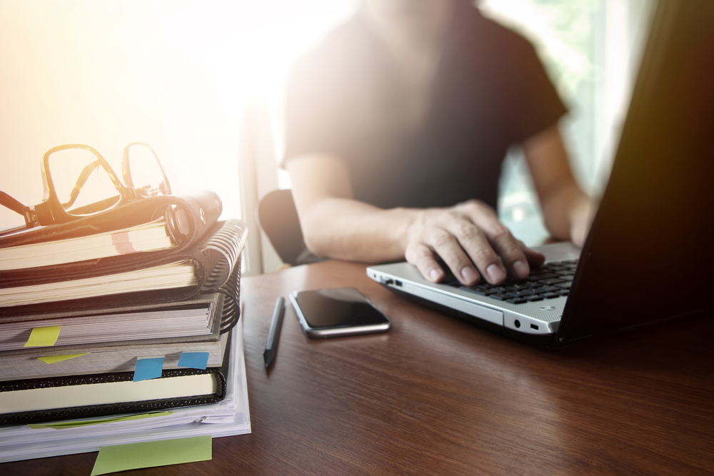 man sitting in front of computer with stack of books