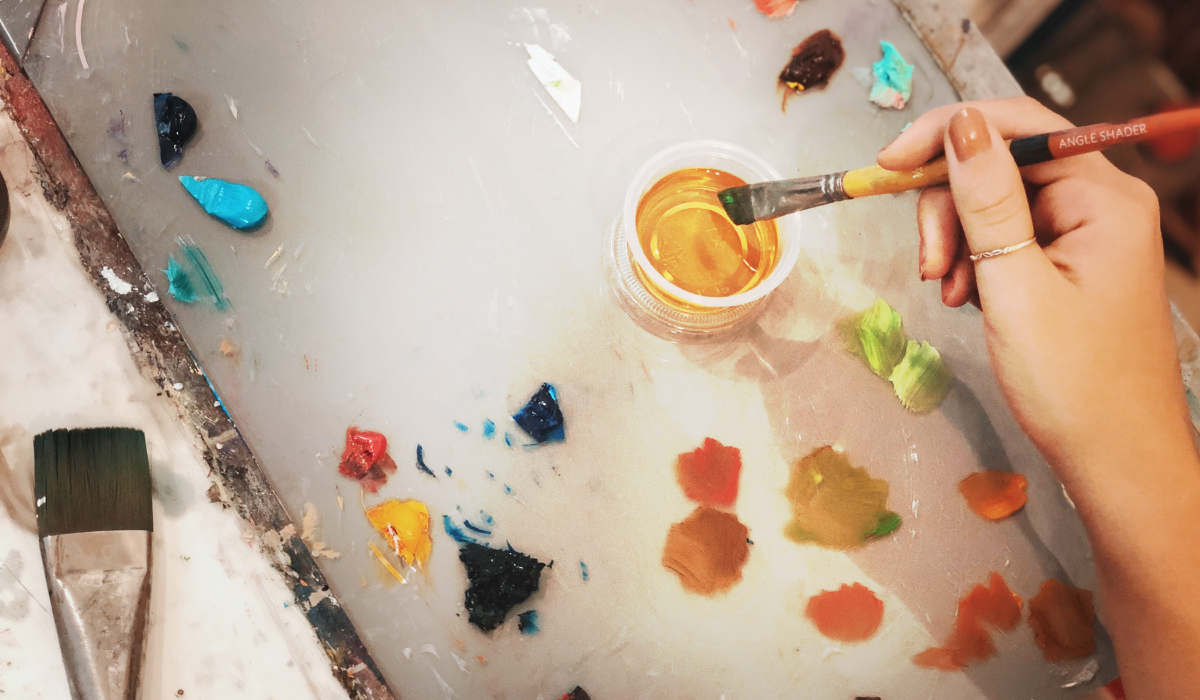 Pallet with paint and paintbrush dipping into medium